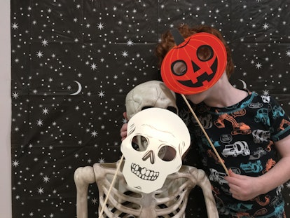 A person holding a cutout of a carved pumpkin up to their face and hugging a skeleton