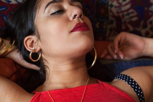 A woman wearing a red crop top and Latinx-inspired jewelry lying on a bed