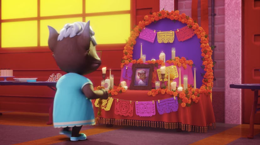A cat from Super Monsters stands in front of an ofrenda for Dia de los Muertos