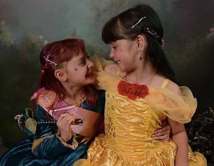 Two sisters in a Belle costume and a princess costume look at each other.