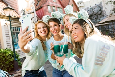 Group of women taking a selfie with aqua-colored Instagrammable Disney drinks at the theme park.