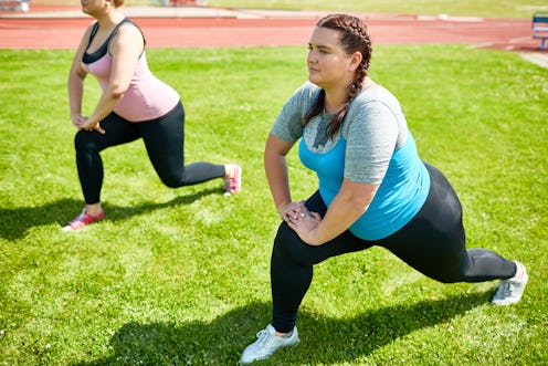 Two people stretching their legs on a grassy track. Personal training can boost your mental health, ...