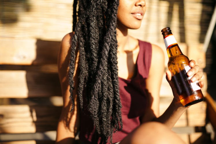 A woman is sitting in the sunshine with a bottle of beer in her hand.