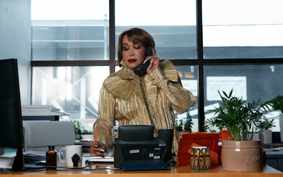 A trans woman executive takes notes while talking on her office phone, standing at her desk. Treatin...
