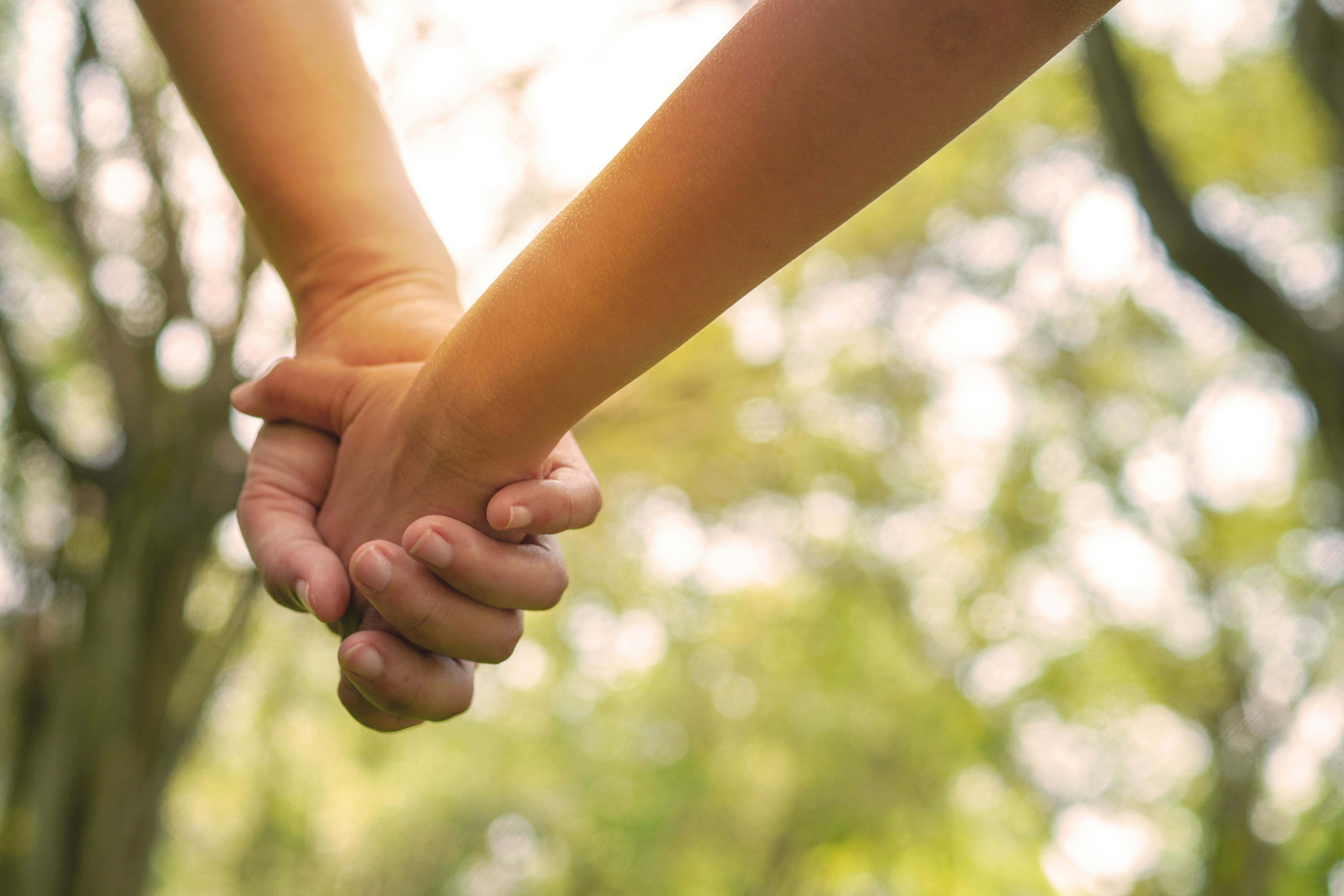 A child holds their parent's hand on the way to school