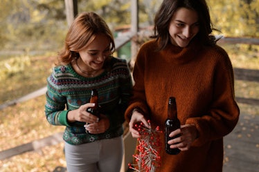 Two women are drinking beer and laughing on a fall day at a cabin.