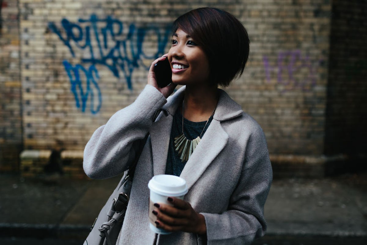 A candid photo of a woman smiling, taking on the phone, and holding a coffee cup in her hand outside would pair well with clever Pumpkin Spice Latte captions.