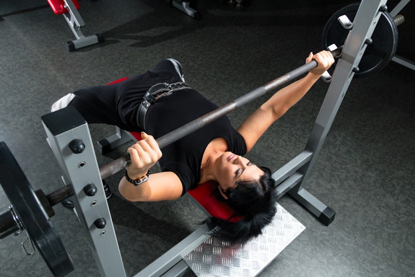 A person wearing a lifting belt prepares to unrack a heavy bench press. Working with a personal trai...
