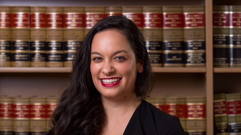A Latinx immigration lawyer, Nubia Batista with a library shelf behind her