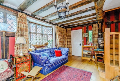 A living room features a bright blue couch, medieval decor, a high ceiling, and long curtains.