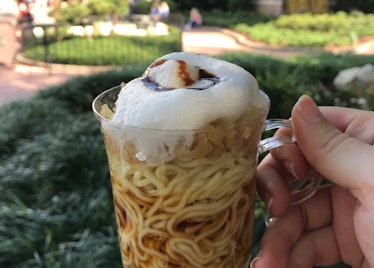 A woman's hand holds up a cup of chilled ramen with froth on top at Disney's Food & Wine Festival at...