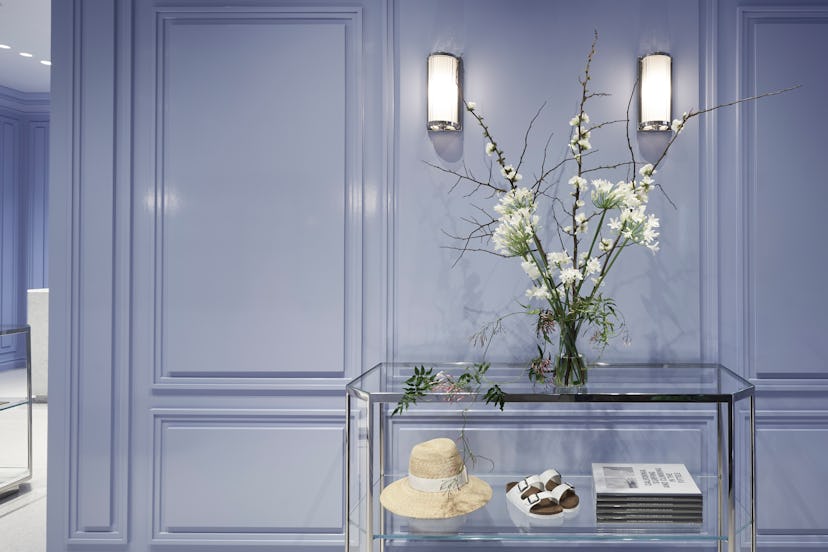Goop's newest store, a glass table, a vase is on top of it with white flowers and a hat, sandals and...