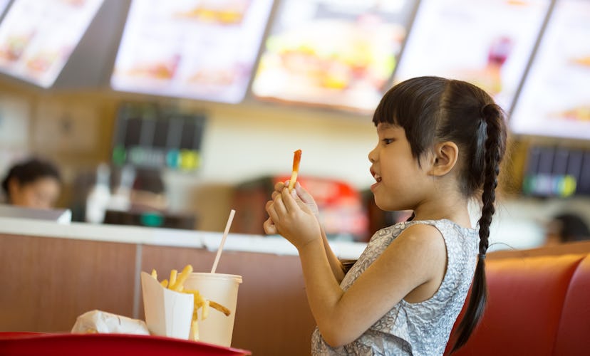 Young girl eats French fries in a food court at a mall