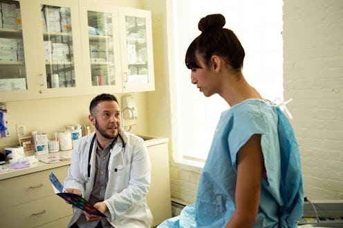 A transgender woman in a hospital gown speaking to her doctor, a transgender man, in an exam room. G...