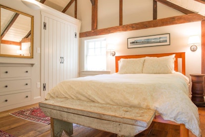 The bedroom of a loft carriage barn apartment in Kennebunkport, Maine has wood details and warm ligh...