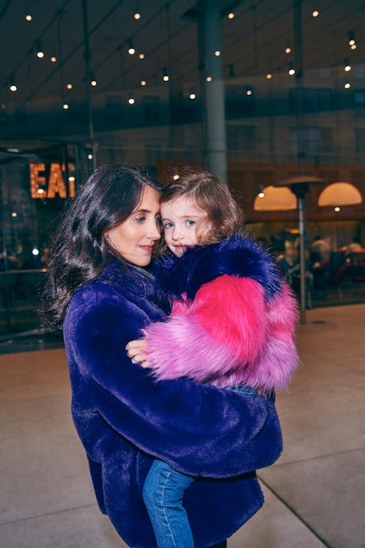 Mother in faux fur coat holds daughter in corresponding jacket