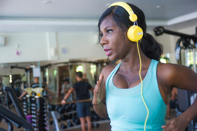 A person with yellow headphones and a blue tank top sweats as she runs on a treadmill. If you're bor...
