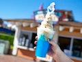 A woman's hand holds up the Olaf Dole Whip Slushy with Olaf from the movie 'Frozen 2' on top.