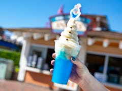 A woman's hand holds up the Olaf Dole Whip Slushy with Olaf from the movie 'Frozen 2' on top.