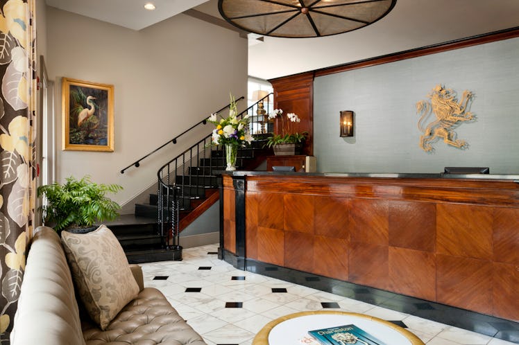 A luxe hotel lobby with a glossy wooden reception desk, marble floors, and a black staircase leading...
