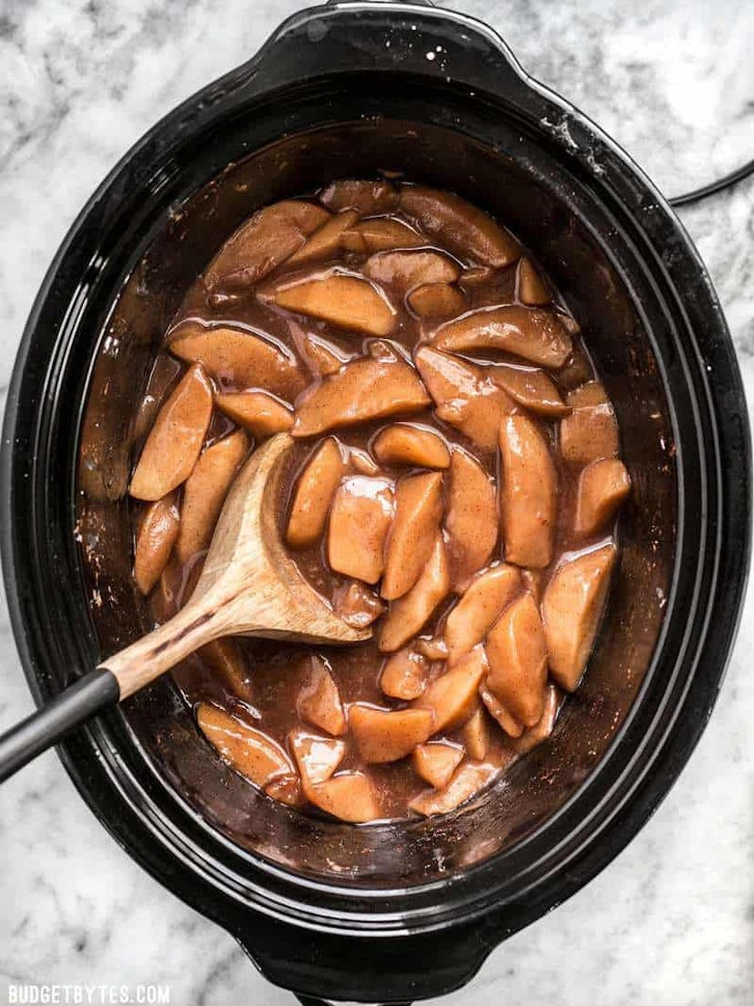 Ariel shot of slow cooker full of gooey, soft, apples in a brown sauce with wooden spoon