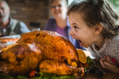 A girl pretends to eat a gigantic turkey at Thanksgiving.