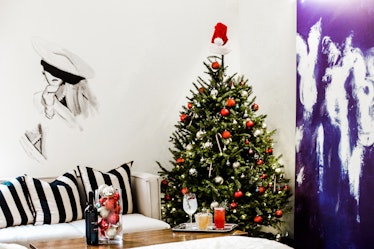 The interior of a hotel room features a decorated Christmas tree next to a white couch with striped ...