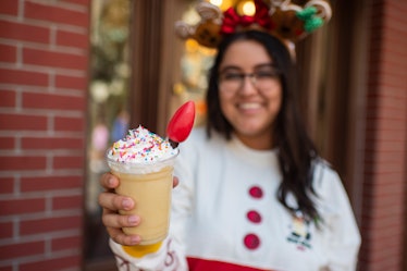 A woman holds out an eggnog milkshake with a light bulb in it, which is available at Mickey's Very M...