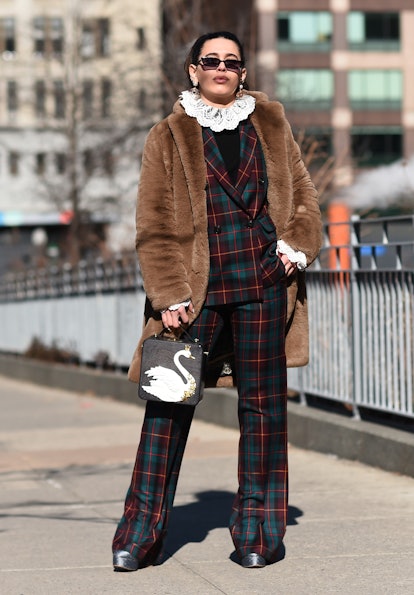 Street style photo of Cici Celia wearing a plaid suit over a ruffle-neck top with a brown fur coat a...