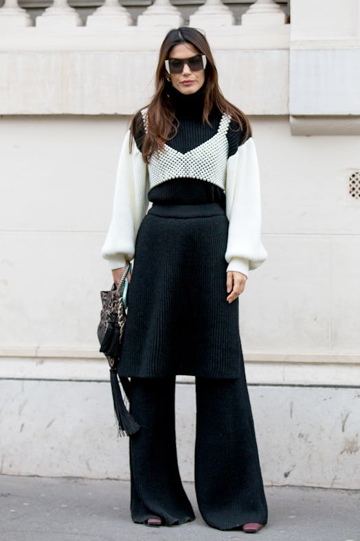 Street style photo of a woman wearing a black and white sweater layered under a pearl tank top with ...