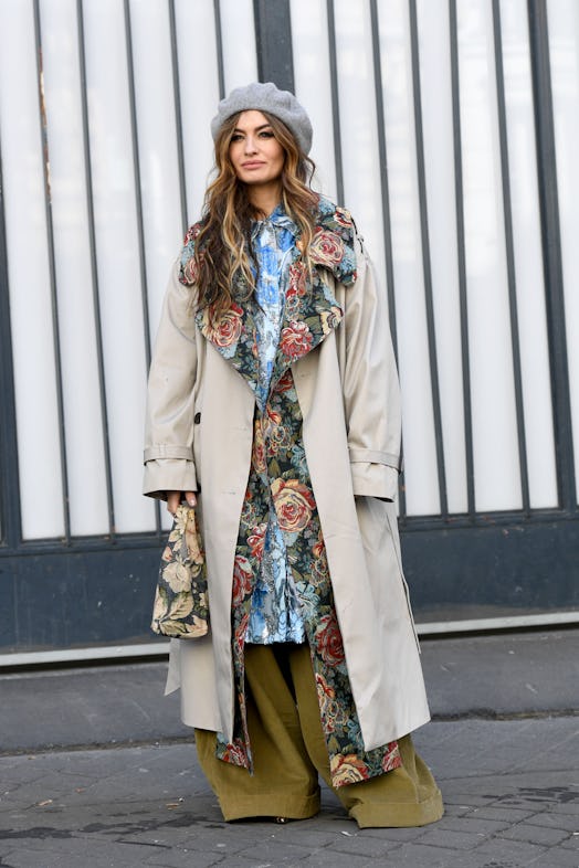Street style photo of a woman wearing a floral shirtdress layered with a floral coat, trench coat, a...