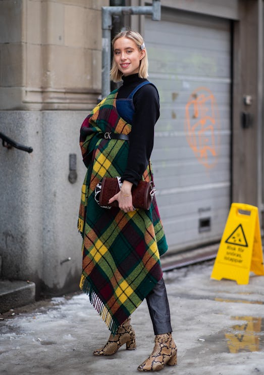 Street style photo of woman wearing a black turtleneck and denim overalls with an oversized plaid sc...