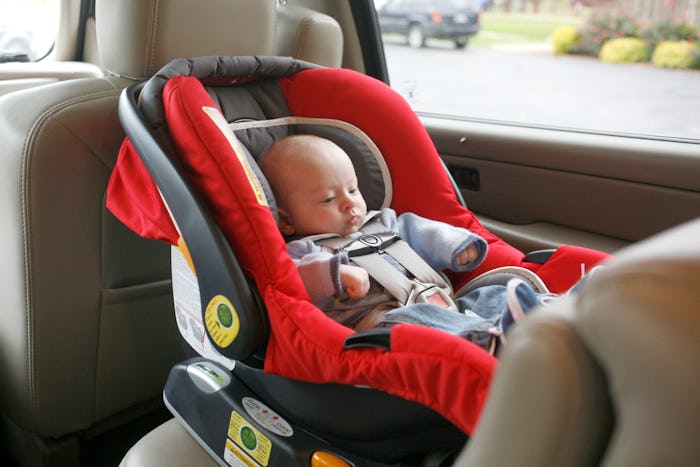 a baby in a light sweater buckled into a car seat