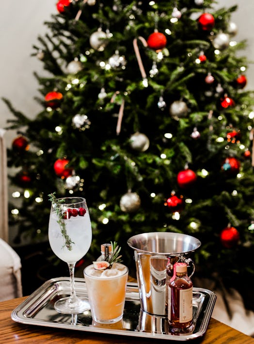 A silver platter of seasonal cocktails sits on a wooden coffee table with a Christmas tree in the ba...