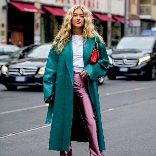 Street style photo of influencer Emili Sindlev wearing a teal leather coat and metallic pink pants a...