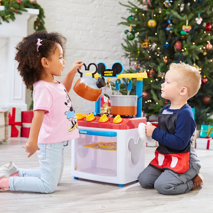 A girl and boy playing with a mickey mouse kitchen from disney