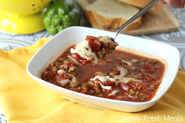 square bowl of red soup with cheese, green and red peppers, chunks of ground meat with spoon scoopin...