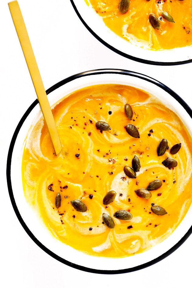 Bright orange butternut squash soup with pumpkin seeds on top in white bowl with orange spoon 