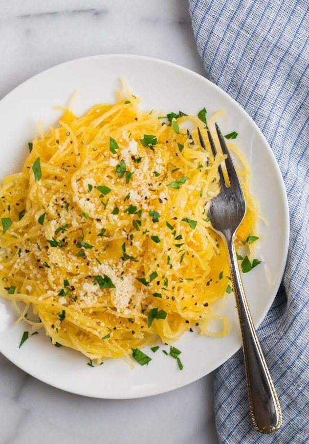 Plate of spaghetti squash garnished with cheese, pepper and parsley on white marble table next to fo...