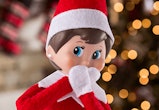 An Elf on the Shelf doll in front of a Christmas tree