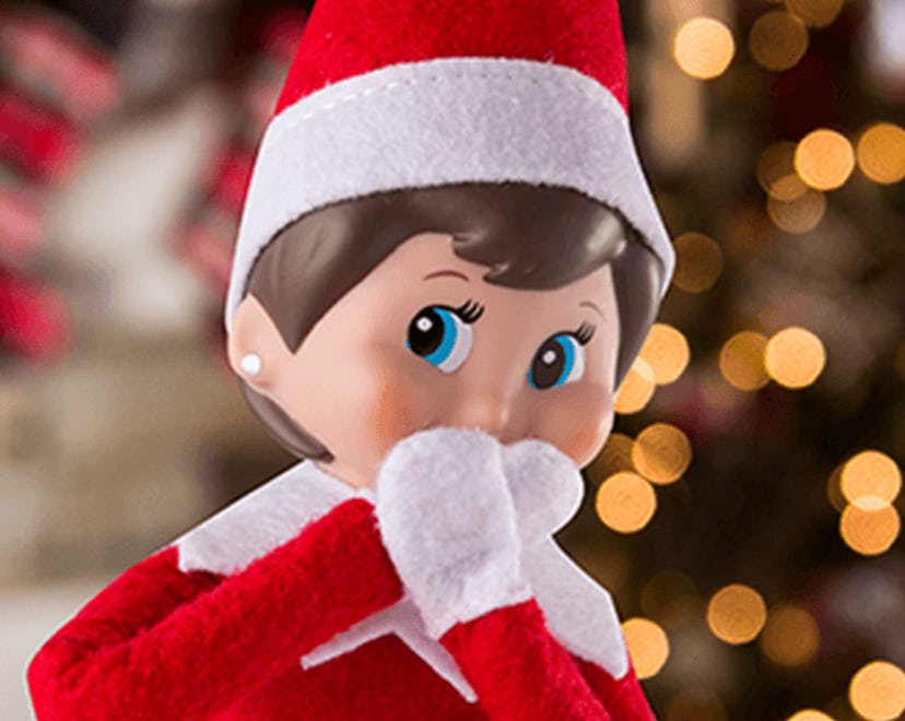 An Elf on the Shelf doll in front of a Christmas tree