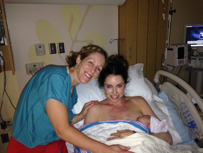woman cradles newborn while nurse smiles