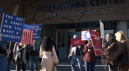 Regina King as Angela Abar walks into the Greenwood Center for Cultural Heritage while people protes...