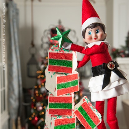 elf on the shelf standing next to a tower of cake bites