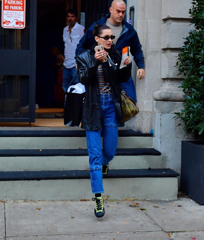 Bella Hadid in a leather blazer, a striped shirt and blue jeans coming down stairs