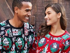 A man and woman wearing coordinating Disney holiday merchandise sweaters smile at each other. 
