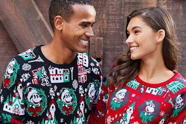 A man and woman wearing coordinating Disney holiday merchandise sweaters smile at each other. 