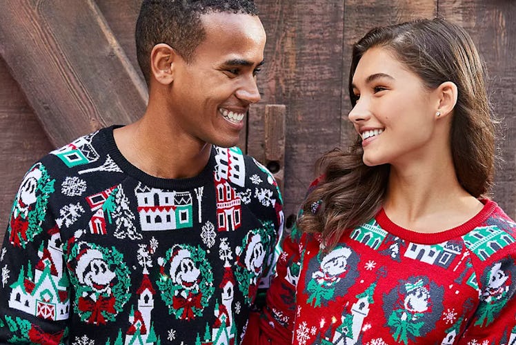 A man and woman wearing coordinating Disney holiday merchandise sweaters smile at each other.