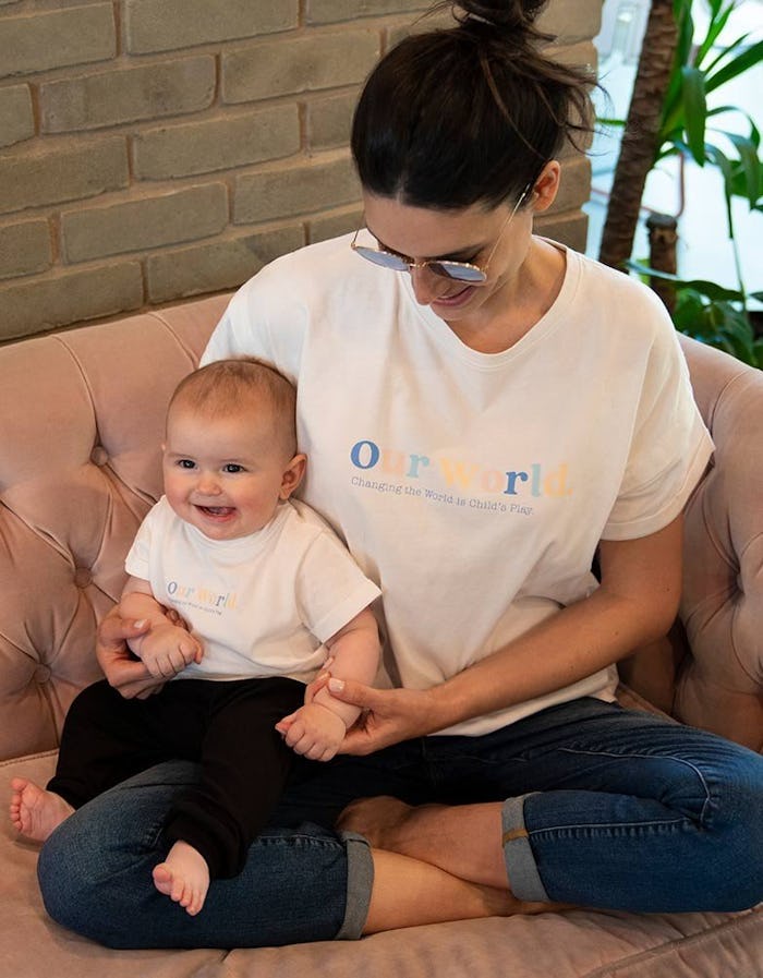 Mom sitting cross-legged with baby in lap, both wearing "our world" t-shirts from seraphine