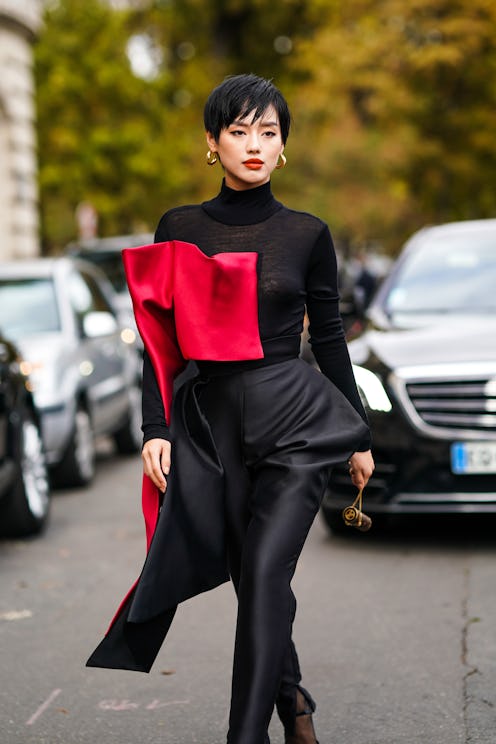 A woman wearing a black dress with red detailing, as well as small gold hoop earrings